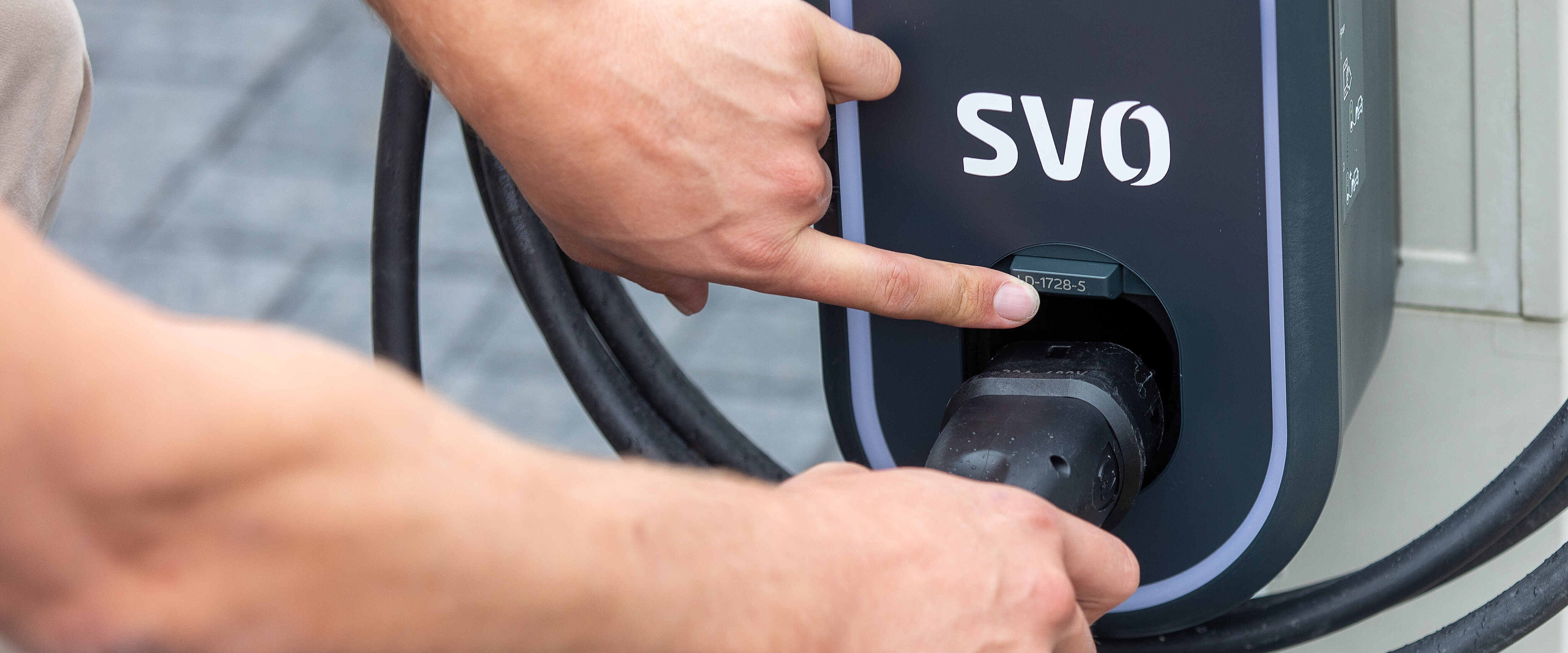 Foto zeigt die Hand einer Person, die einen Ladestecker in die Buchse eines Elektroautos steckt. 