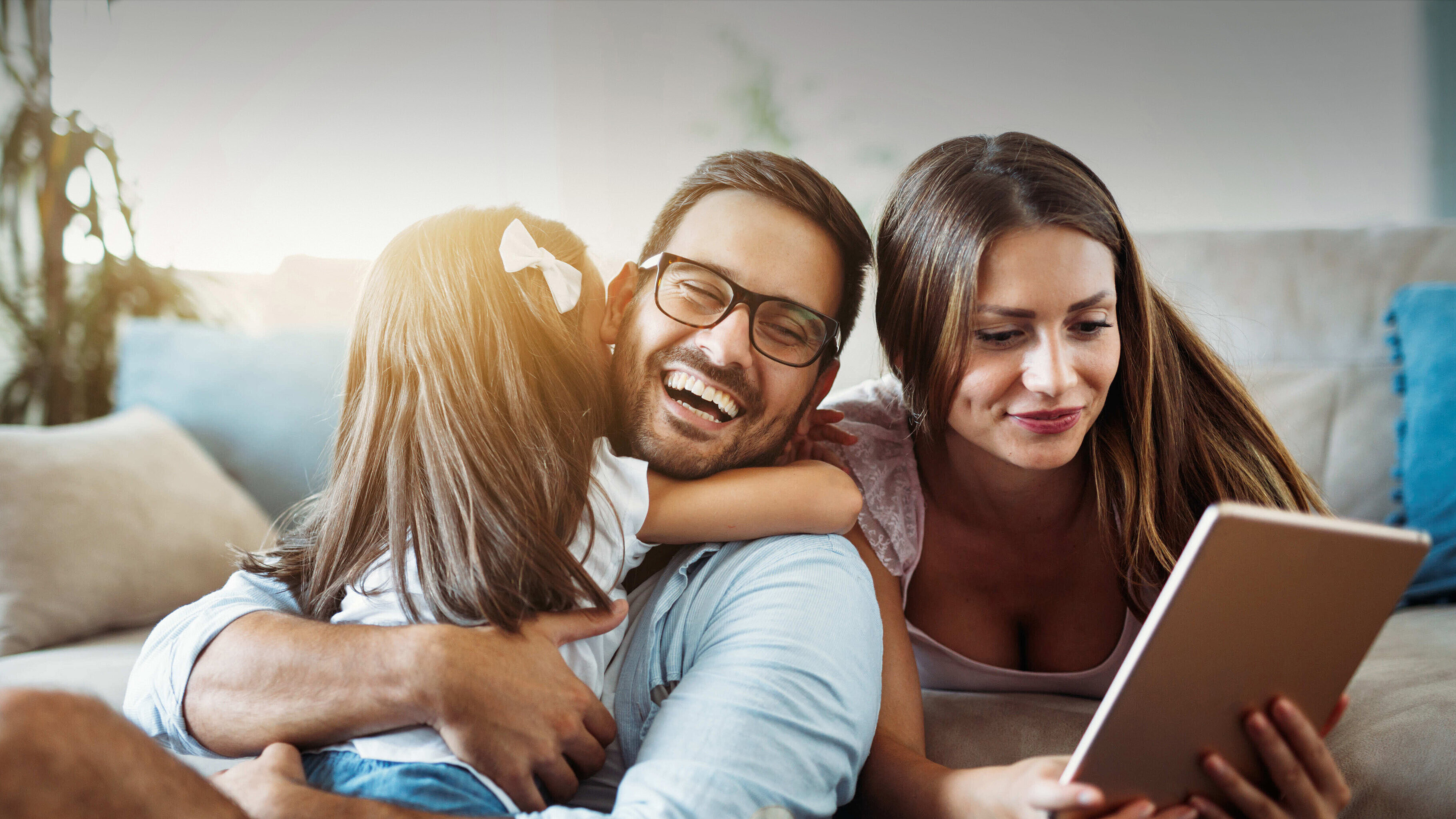 Familie SVO Kunden Ein junger Mann und eine junge Frau sitzen und liegen mit ihrem kleinen Kind auf dem Sofa und schauen auf ein Tablet.